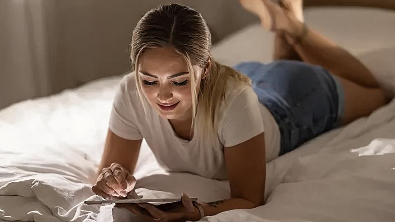 Getty Images A young blonde woman lying on a bed looking at a tablet