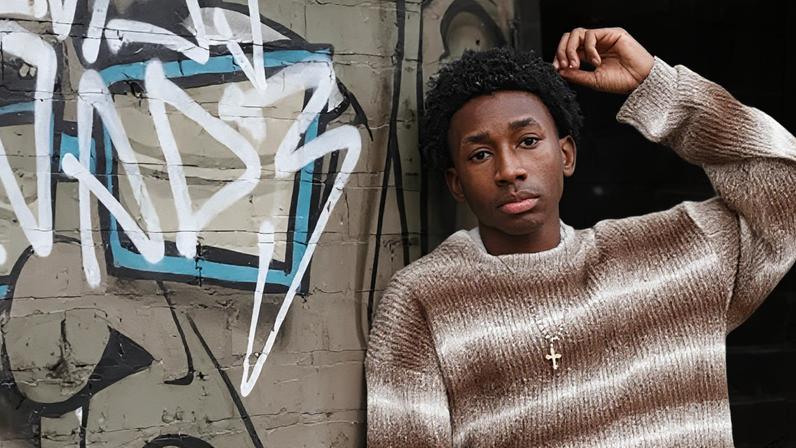 Ziame Stewart A boy with black curly hair poses against a graffitied wall