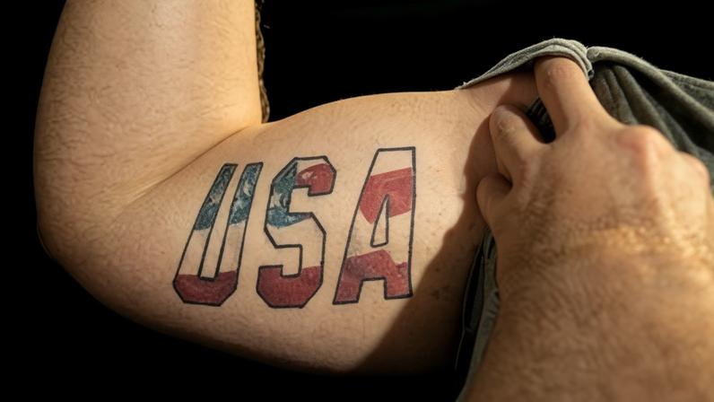 A man flexing his bicep demonstrates a U.S.A. tattoo in red, white and blue.