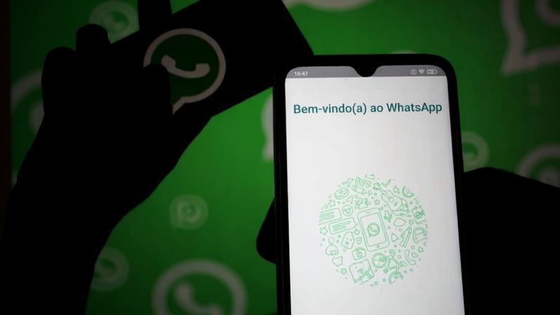 foto colorida com silhueta de mão segurando celular com logo do whatsapp e outra mão segurando a tela de bem-vindo ao whatsapp - metrópolea