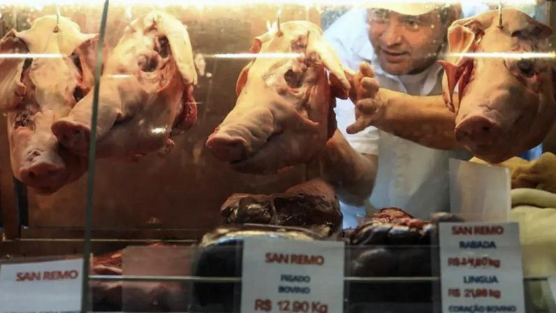 Trabalhador mexe em uma cabeça de porco pendurada em um açougue