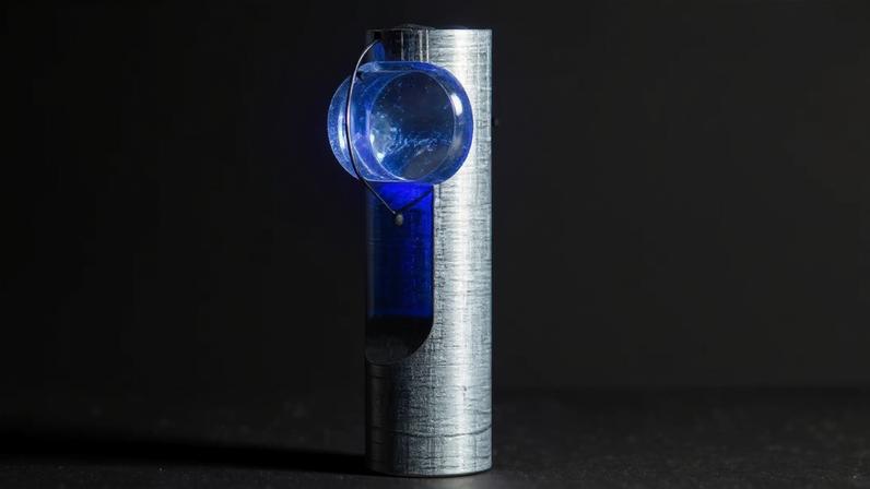 Um pequeno LED azul brilhante, preso por um fio fino a uma haste metálica texturizada, projeta luz intensa sobre a superfície da haste, criando um reflexo azul vibrante