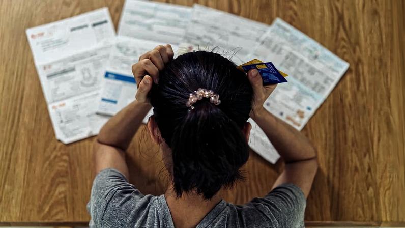Vista superior de uma jovem asiática estressada com as mãos segurando a cabeça preocupada em encontrar dinheiro para pagar dívidas de cartão de crédito e todas as contas de empréstimo. Conceito de problema financeiro.