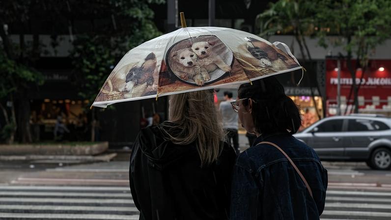 Mulheres se protegendo da chuva na avenida Paulista; instabilidade deve seguir até o fim de semana