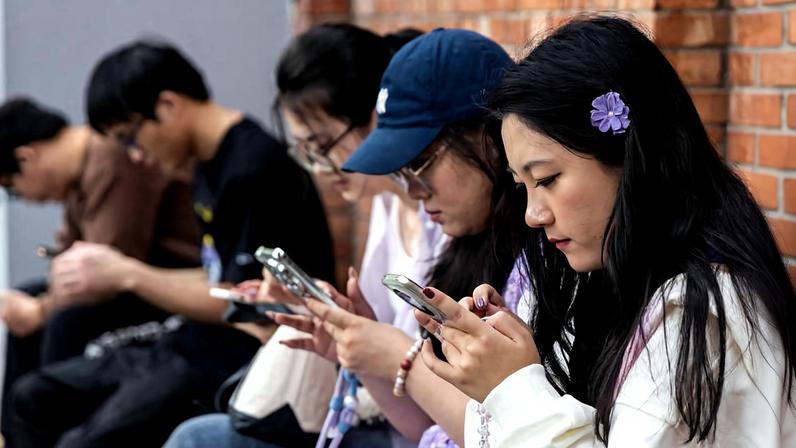 Jovens usando telefone sentados em banco em distrito de Pequim, na China