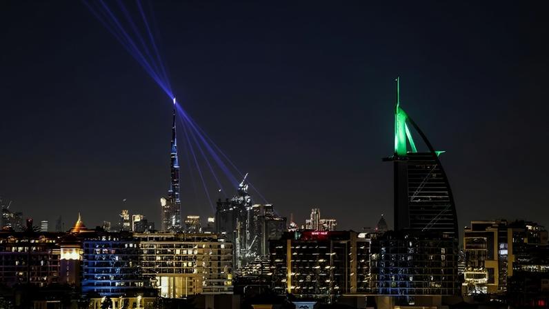 Vista noturna da cidade de Dubai com o Burj Khalifa emitindo feixes de luz roxos para o céu e o Burj Al Arab iluminado em verde. Edifícios modernos e luzes urbanas compõem o cenário.