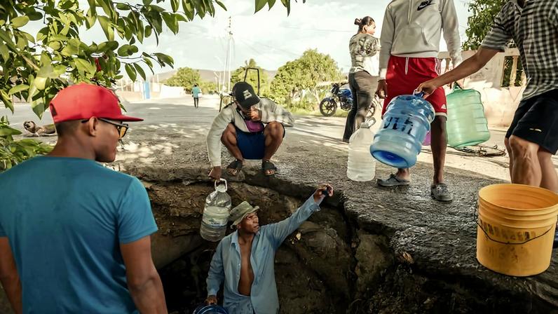 Homens em Cumaná, na Venezuela, recolhem água de um riacho poluído