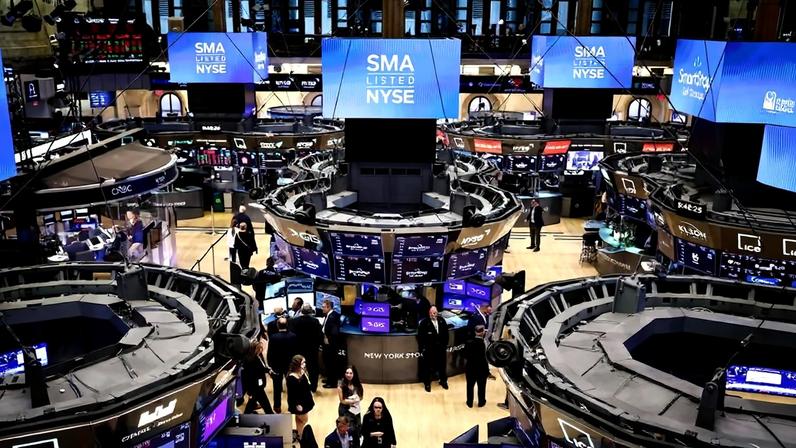 Área principal da Bolsa de Valores de Nova York com operadores em pé e caminhando entre estações de negociação circulares. Múltiplas telas digitais exibem informações financeiras e o texto 'SMA LISTED NYSE'. Ambiente interno com iluminação artificial e estrutura arquitetônica visível ao fundo.