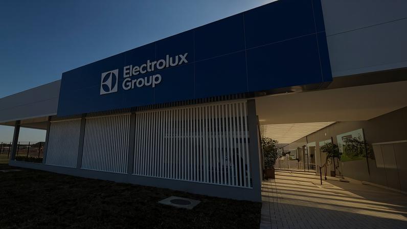 Fachada moderna da sede da Electrolux Group com estrutura azul e branca, em área externa com céu claro e gramado ao redor