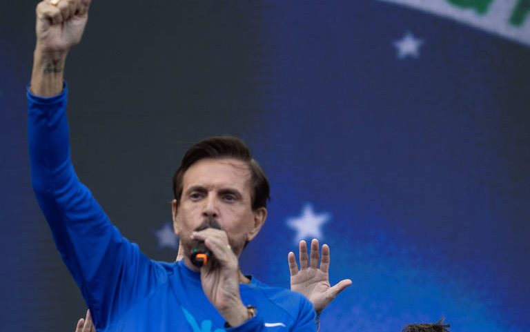 34ª Marcha para Jesus. Bispo Estevam Hernades fala ao público com Flávio Bolsonaro ao fundo no palco.