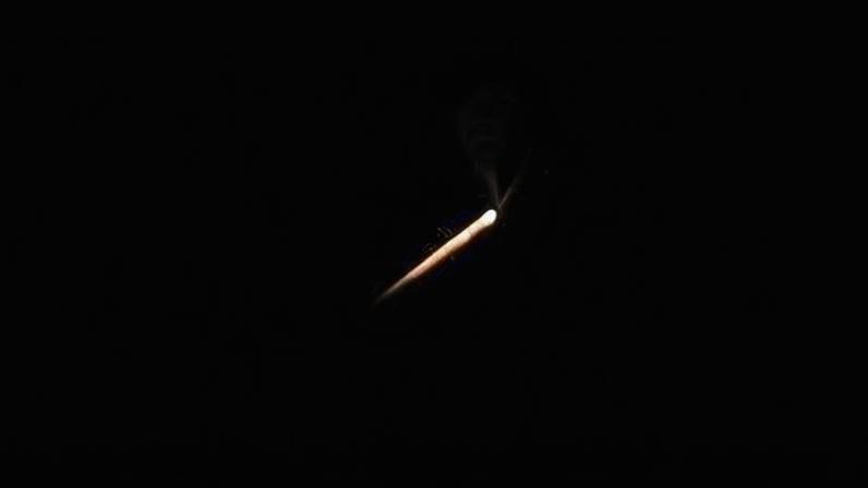 Rastro luminoso alaranjado e branco corta o céu escuro, indicando objeto em movimento rápido.