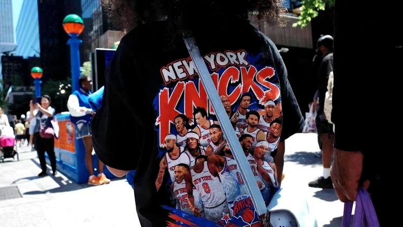 Vestindo camiseta dos Knicks, pessoas passam ao lado de entrada da estação de metrô 34, Penn Station, decorada com as cores do time, na cidade de Nova York