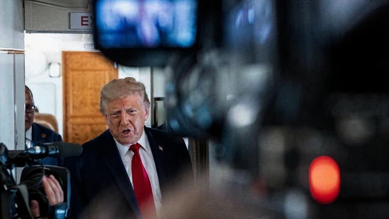 Donald Trump, ex-presidente dos EUA, fala diante de câmeras e microfones em ambiente interno, possivelmente um corredor ou sala de embarque.