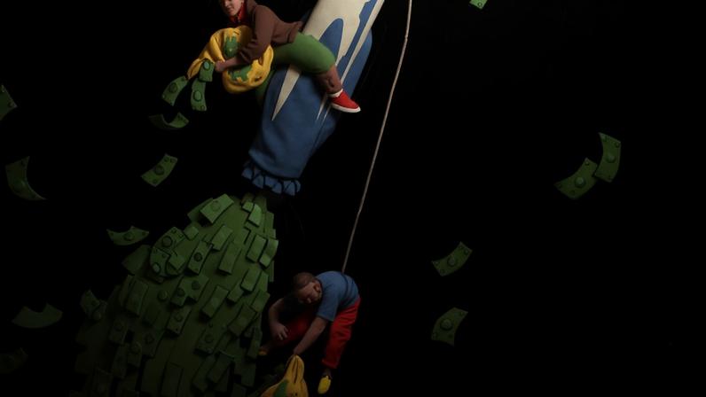 Seis pessoas escalam um lápis gigante na vertical contra fundo preto. Dinheiro em cédulas verdes cai ao redor e uma pilha de dinheiro está no chão abaixo do lápis.
