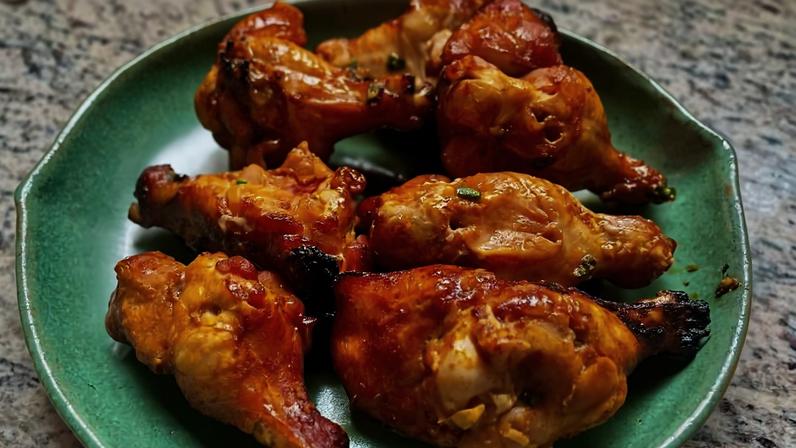 Seis pedaços de frango assado com pele dourada e levemente tostada, dispostos em prato verde sobre superfície de mármore.