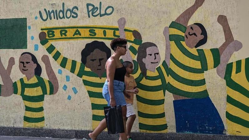 Mulher e criança passam em frente a mural preparado para a Copa de 2026 no Rio de Janeiro