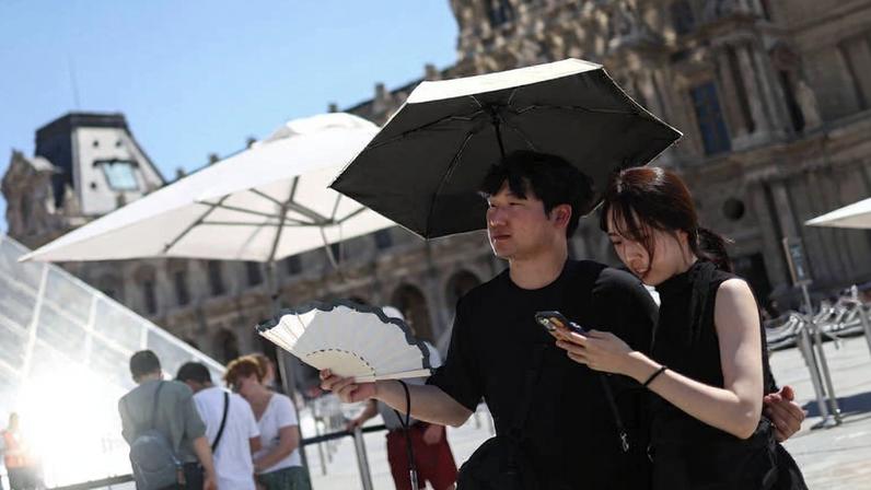 Duas pessoas se abrigam sob um guarda-chuva e usam um leque do lado de fora do Louvre em meio a uma forte onda de calor em Paris, na França