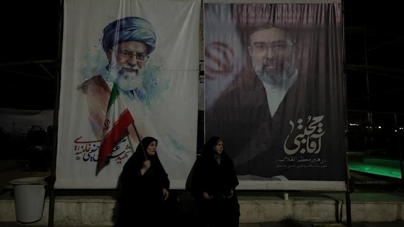 Duas mulher, uma delas com a bandeira iraniana, diante de retratos do ex-líder supremo do Irã Ali Khamenei e de seu sucessor, seu filho Mojtaba Khamenei, durante uma manifestação pró-regime em Teerã
