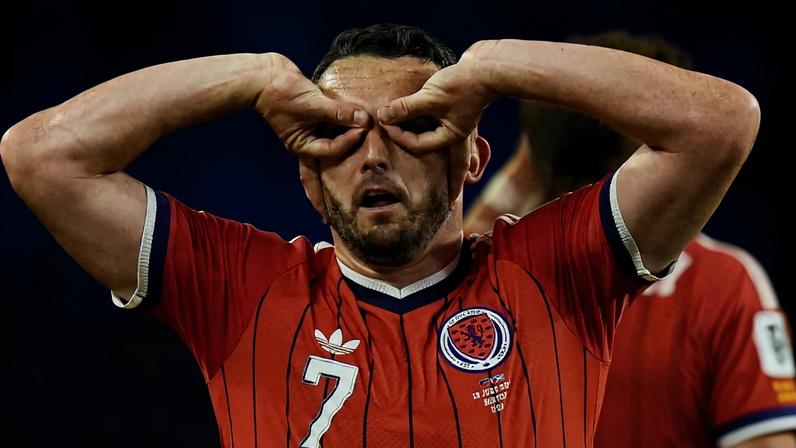 Jogador com camisa vermelha número 7 faz gesto com as mãos simulando óculos ao redor dos olhos durante partida.