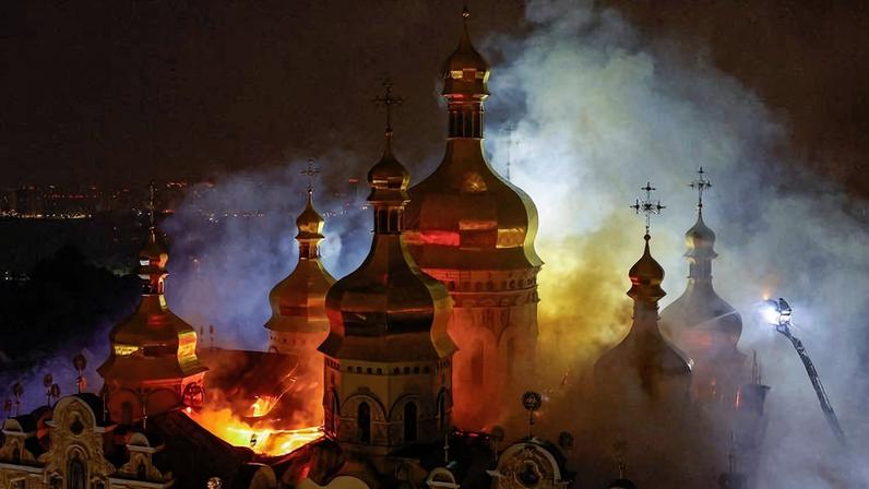 Chamas e fumaça envolvem cúpulas douradas de igreja ortodoxa durante incêndio noturno. Bombeiros atuam com jato de água para controlar fogo.