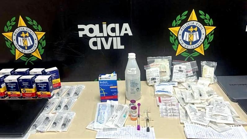 Mesa com caixas de medicamentos, seringas, frascos, ampolas, papéis e cadernos organizados. Fundo com logotipos da Polícia Civil em preto, verde e amarelo.
