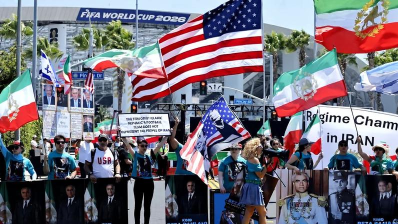 Manifestantes exibem antiga bandeira do Irã e pôsteres pedindo retorno de Reza Pahlavi aos arredores do estádio SoFi; cartaz diz que "o time de futebol da terrorista República Islâmica não representa o povo do Irã
