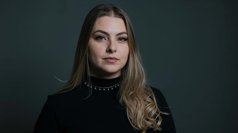 Raphaela em 'selfie'. Ela é loira, tem olhos azuis, e olha diretamente para a câmera, com um sorriso sutil.