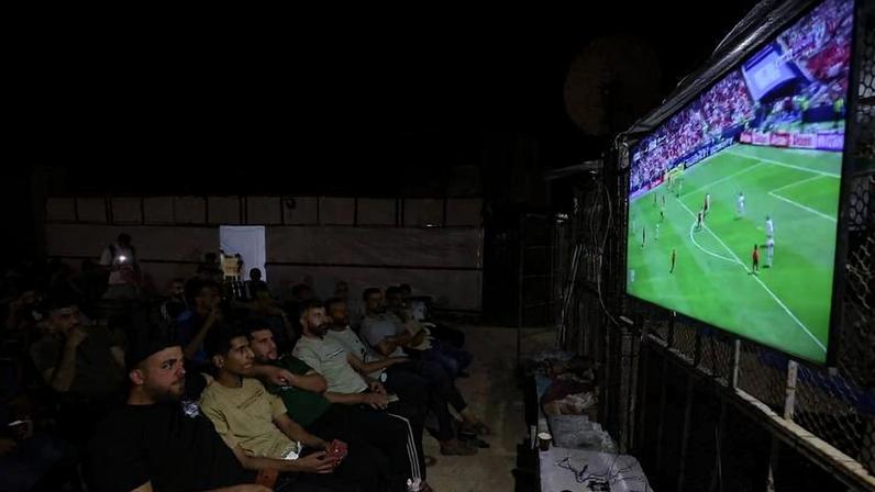 Palestinos assistem à partida entre Bélgica e Egito, da Copa do Mundo, em telão no campo de refugiados de Nuseirat, na Faixa de Gaza