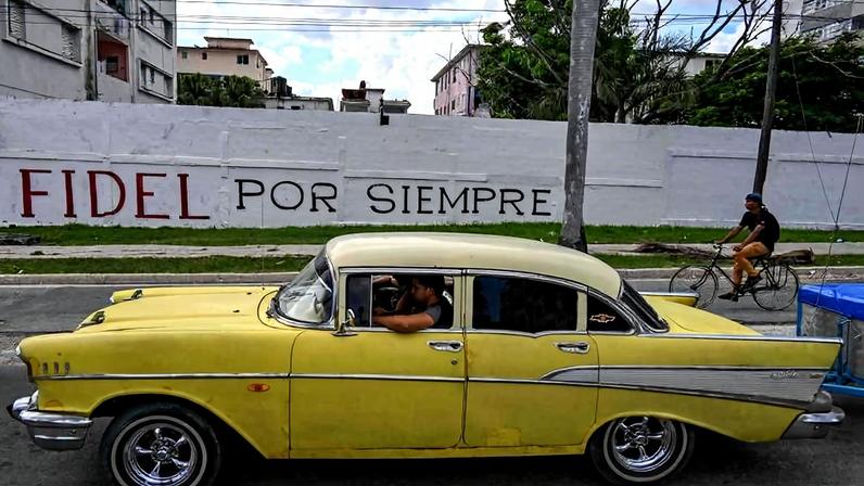 Carro antigo passa na frente de uma parede com a inscrição "Fidel para sempre", em Havana
