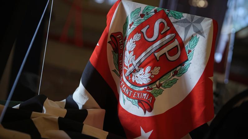Lenço com as cores vermelho, branco e preto, exibindo o brasão do São Paulo Futebol Clube com as letras 'SP' em destaque e a frase 'Non ducor, duco'.