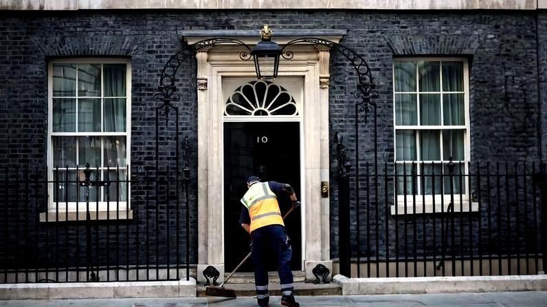 Gari varre a calçada em frente ao número 10 de Downing Street, sede do governo britânico, na manhã desta segunda-feira (22), enquanto jornalistas aguardam pronunciamento de Keir Starmer