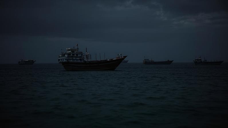 Quatro barcos de diferentes tamanhos flutuam no mar calmo com céu cinza ao fundo. O barco maior está mais próximo, com estrutura branca e casco escuro, enquanto os outros três estão mais distantes e alinhados horizontalmente.