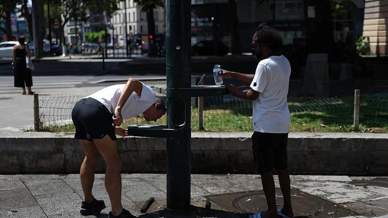 Pessoas bebem água em uma fonte em uma rua de Paris enquanto as temperaturas sobem durante uma onda de calor que afeta grande parte da França