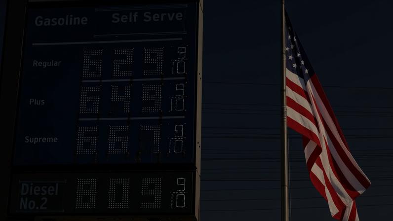 Painel de preços de um posto de gasolina ao lado de uma bandeira dos EUA em El Segundo, na Califórnia