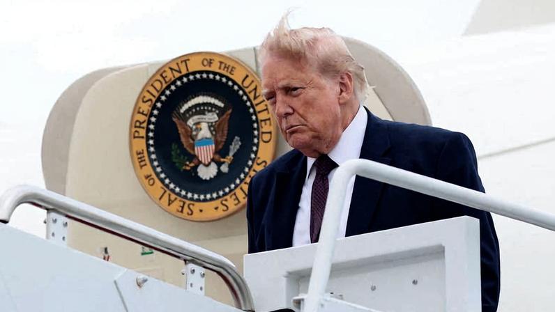 Homem de terno escuro e gravata vermelha desce escada de avião com selo presidencial dos Estados Unidos ao fundo.