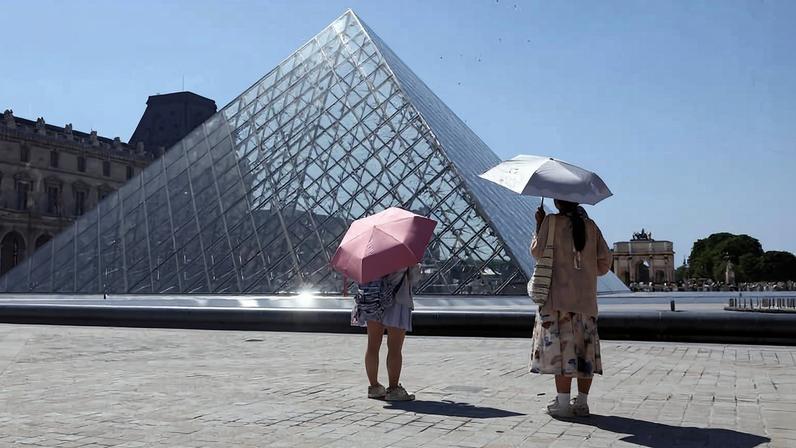 Turistas usam guarda-chuva para se proteger de calor em frente ao Louvre, em Paris