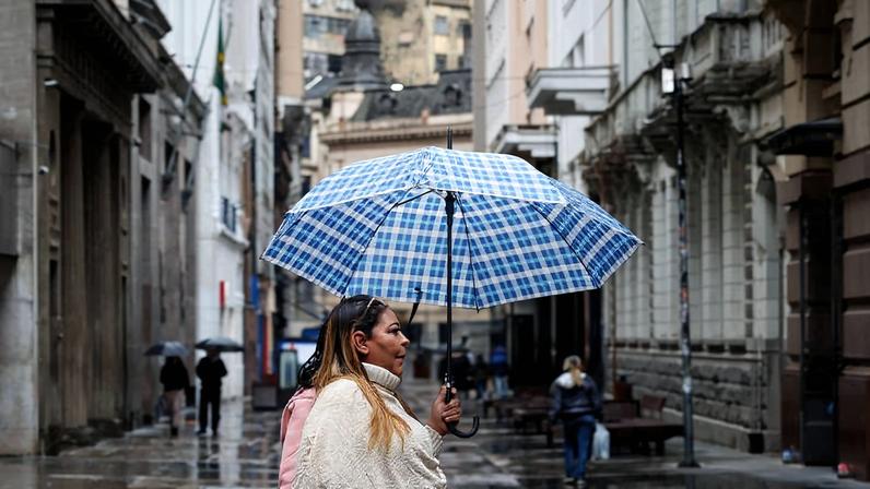 Pedestre se protege da chuva e do frio na região da rua 15 de Novembro, no centro da SP