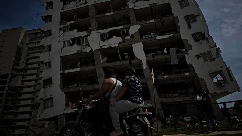 Duas pessoas passam de moto por um prédio de apartamentos gravemente danificado em Catia La Mar, a cerca de 30 km de Caracas