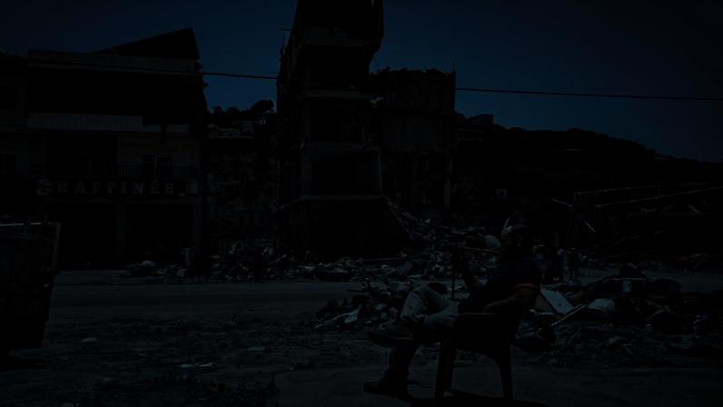Homem sentado diante de prédios destruídos por ataques israelenses em Nabatieh, no sul do Líbano