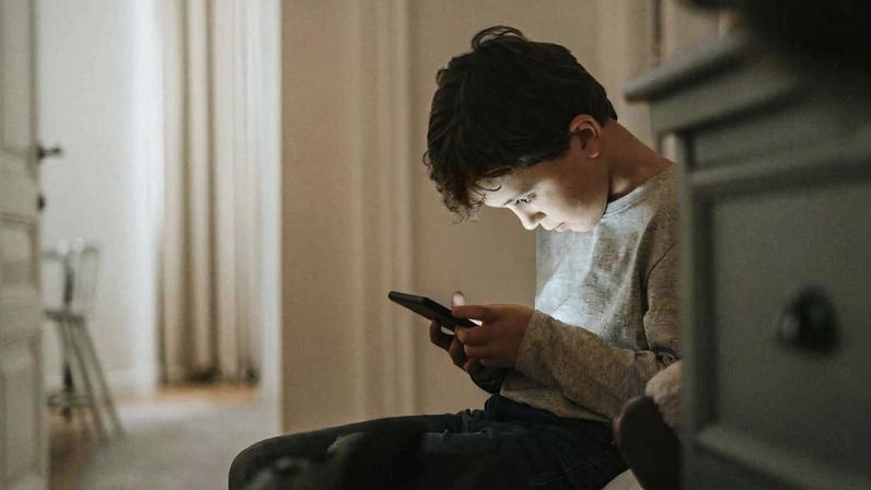 Menino olhando concentrado para o celular em casa: modelo de negócios das redes sociais é estruturado para maximizar atenção, explica especialista