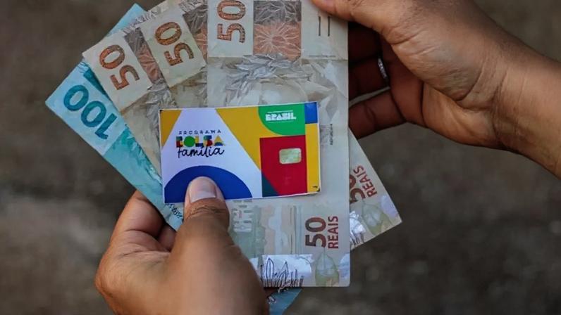 Pessoa segurando cartão do Bolsa Família e benefício.