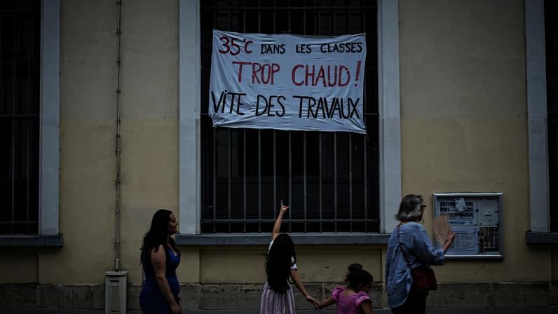 Menina aponta cartaz em escola de Paris que denuncia calor de 35°C nas salas de aula, em 18 de junho de 2026.