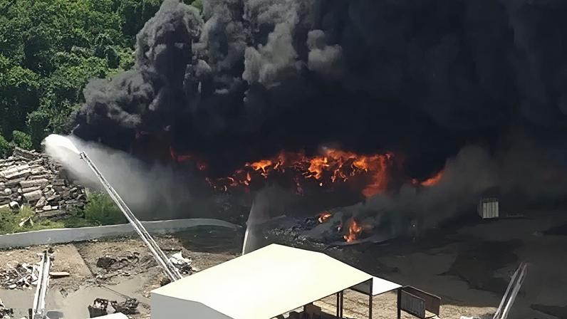 A large plume of black smoke rises from a fire as a fire engine sprays a large jet of water toward it.