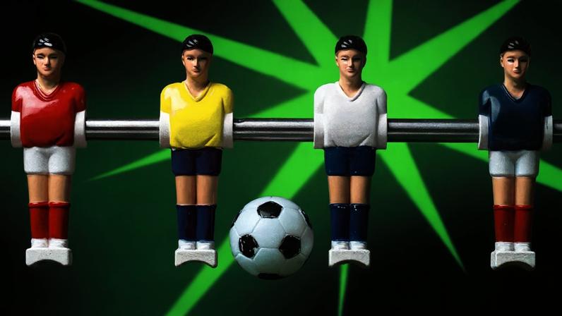 Quatro jogadores de futebol de mesa alinhadas em uma vara com uma bola de futebol no meio sobre um fundo verde elétrico.
