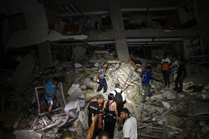 Pessoas caminham sobre os escombros perto de um prédio danificado após um terremoto em Catia La Mar, no estado de La Guaira — cerca de 30 km a noroeste de Caracas —, nas primeiras horas de 25 de junho de 2026 - (crédito: FEDERICO PARRA / AFP)