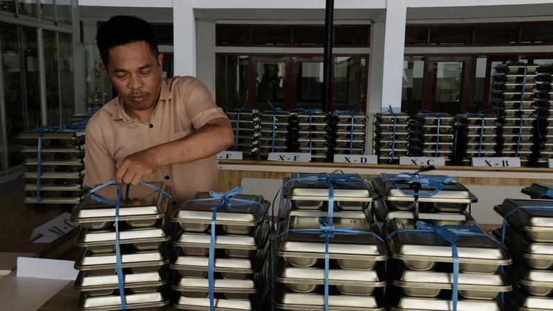A school officer carries free meals to be distributed among high school students in West Java, Indonesia, in 2025.
