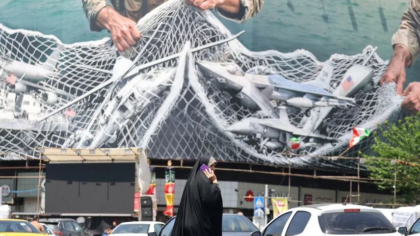 A woman walks past a giant billboard reading "The Strait of Hormuz remains closed" in Tehran.