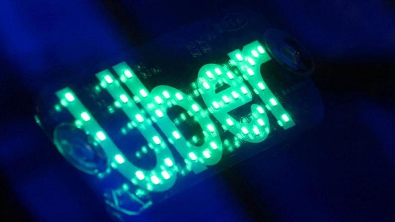 Sinal Uber com LEDs verdes, sobre fundo escuro.