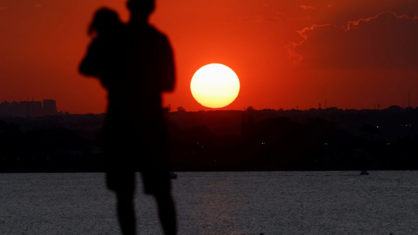 Um homem segura uma criança em Brasília durante o pôr-do-sol de quarta-feira (20); Brasil vive onda de calor. — Foto: Adriano Machado/Reuters