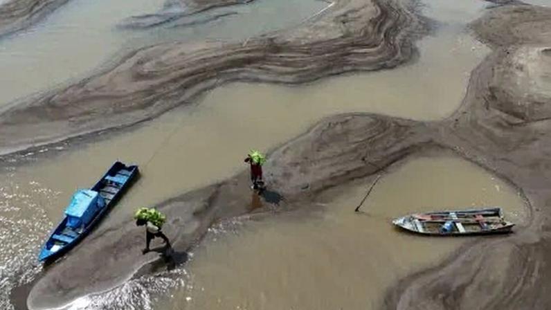 Pessoas carregam bananas caminhando sobre bancos de areia em meio à seca que afetou o Rio Solimões, em Manacapuru, no Amazonas, em setembro de 2024